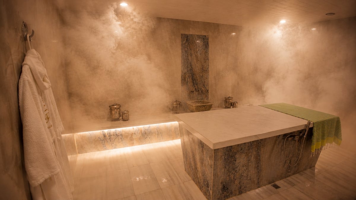 Luxurious bathroom with warm lighting, sunken stone bathtub, lit vanity mirror, and towel rack
